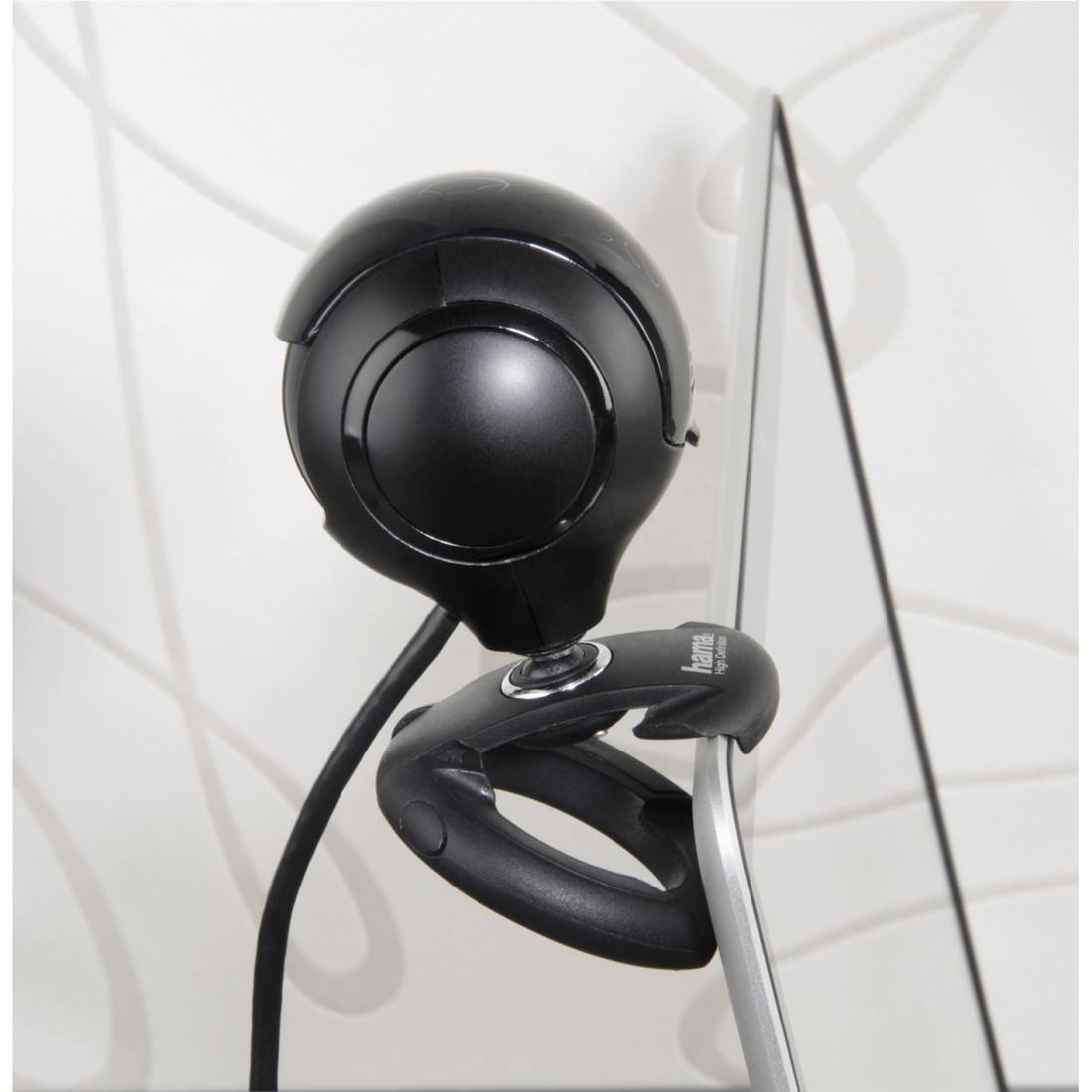 Een ronde, zwarte webcam is bevestigd op een computerscherm. Op de achtergrond is een abstract patroon zichtbaar.