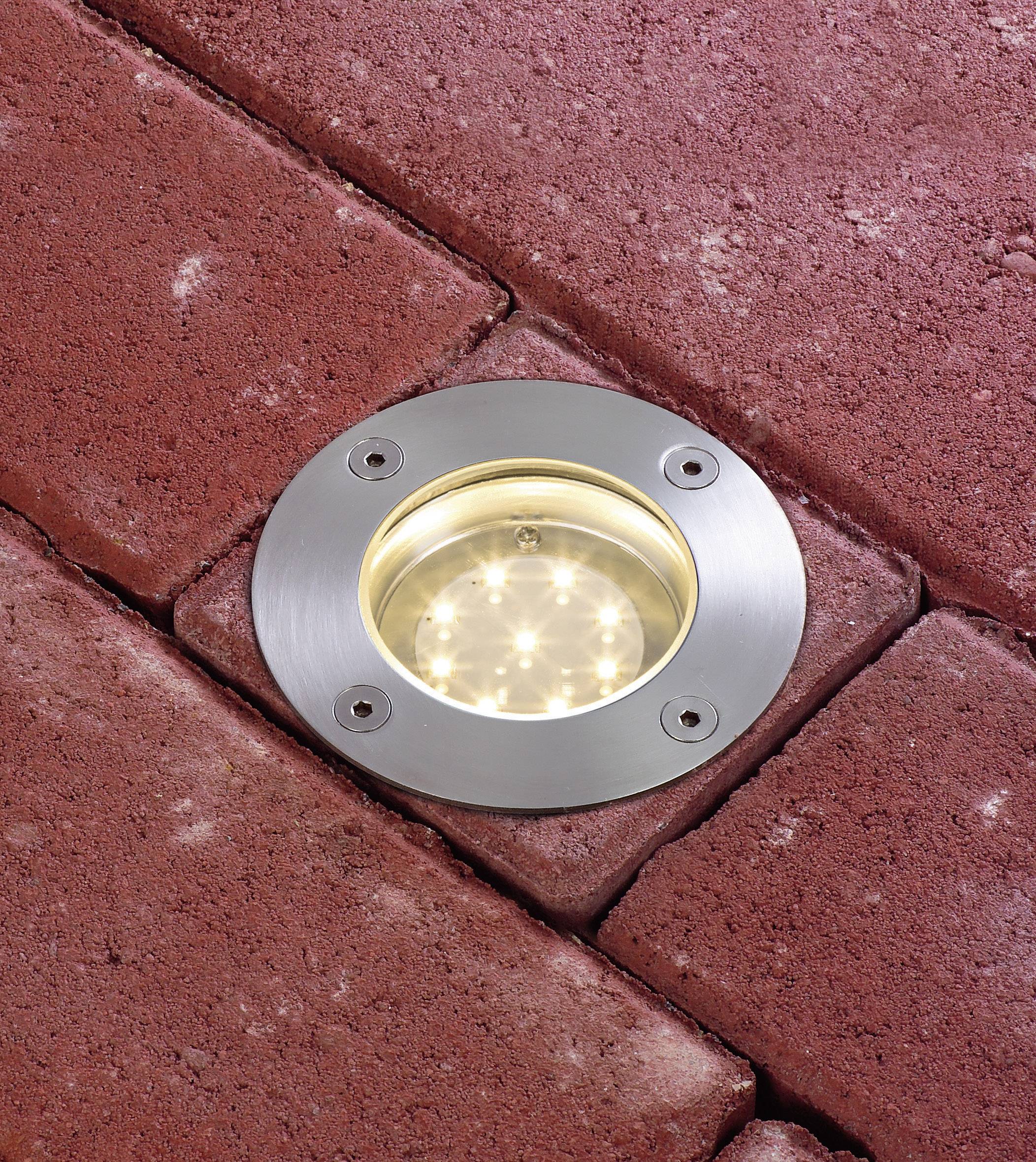 Een ronde vloerlamp is ingewerkt in rode bestratingstegels. Hij verlicht met meerdere kleine LED-lampjes.