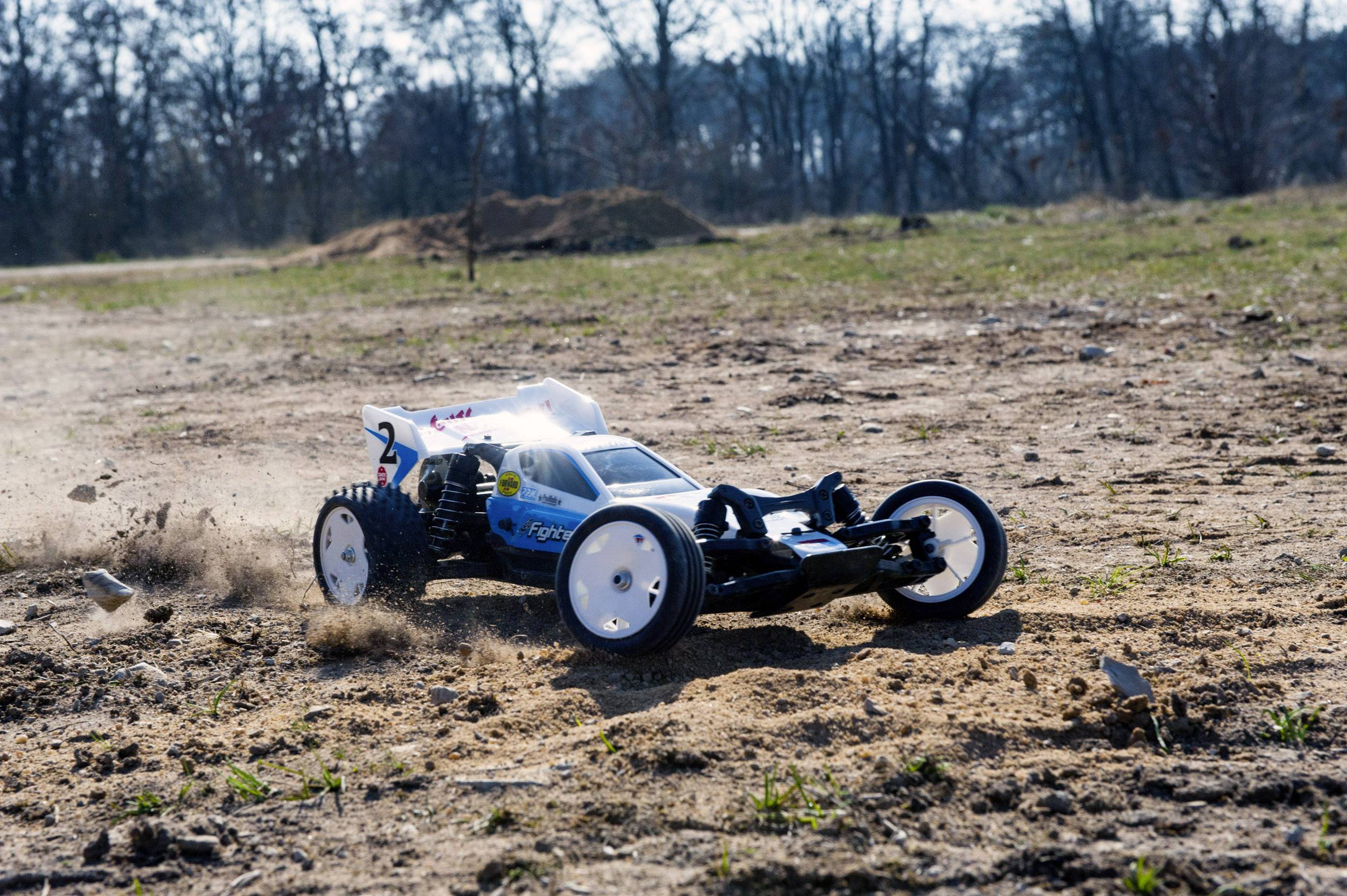 Een afstandsbediende auto rijdt snel over een stoffige, oneffen oppervlakte en werkt stof op. Op de achtergrond zijn bomen zichtbaar.