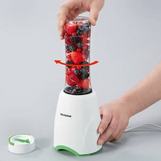 Een persoon vult een blender met bessen. De blender is wit met een groene accent. Een hand houdt het deksel vast. Het mengproces wordt gedemonstreerd.
