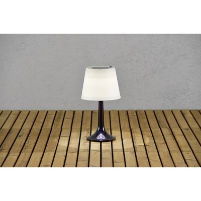 Een enkele tafellamp met een witte lampenkap staat op een houten vloer voor een grijze muur.
