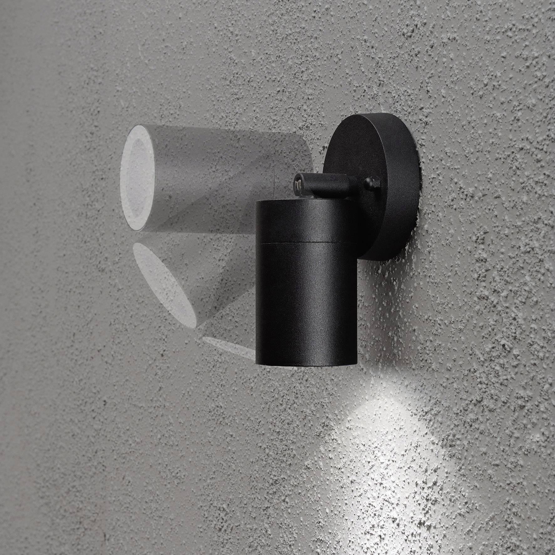 Zwarte wandlamp op een grijze, gestructureerde oppervlakte, werpt gefocust licht naar beneden.