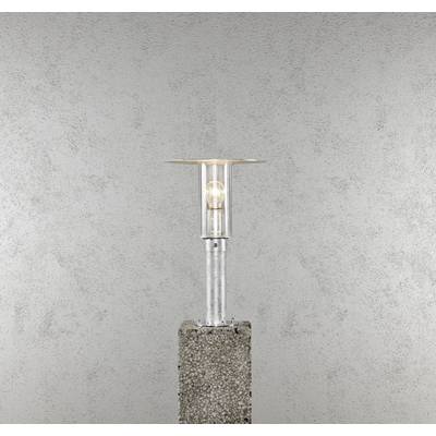 Een moderne, transparante staande lamp met een cilindrische glazen kap, gemonteerd op een betonnen blok, staat voor een grijze muur.