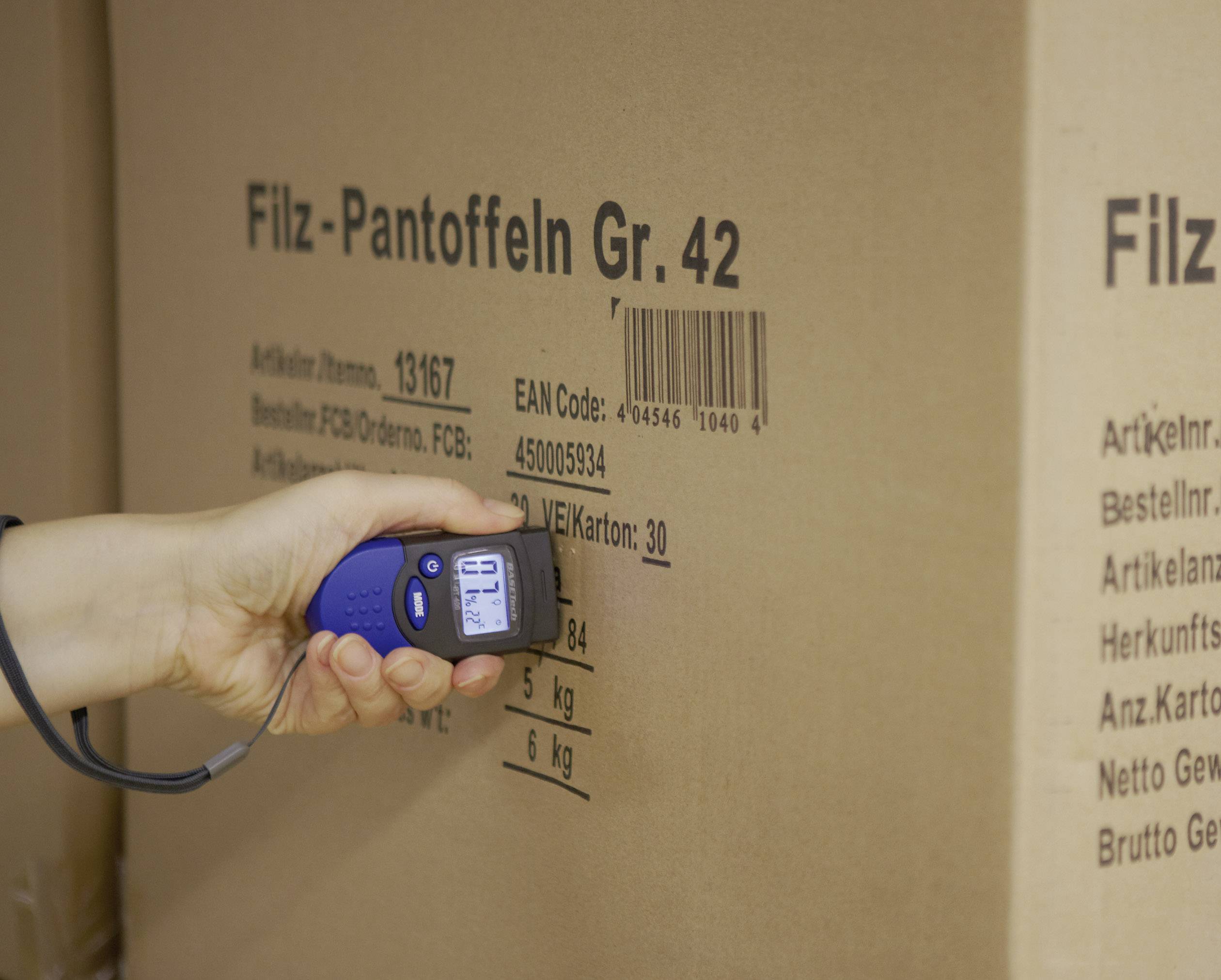 'Hand houdt een apparaat tegen een karton met de opdruk: Vilt-pantoffels Maat 42. Barcode en gewicht van 6 kg zijn zichtbaar.'