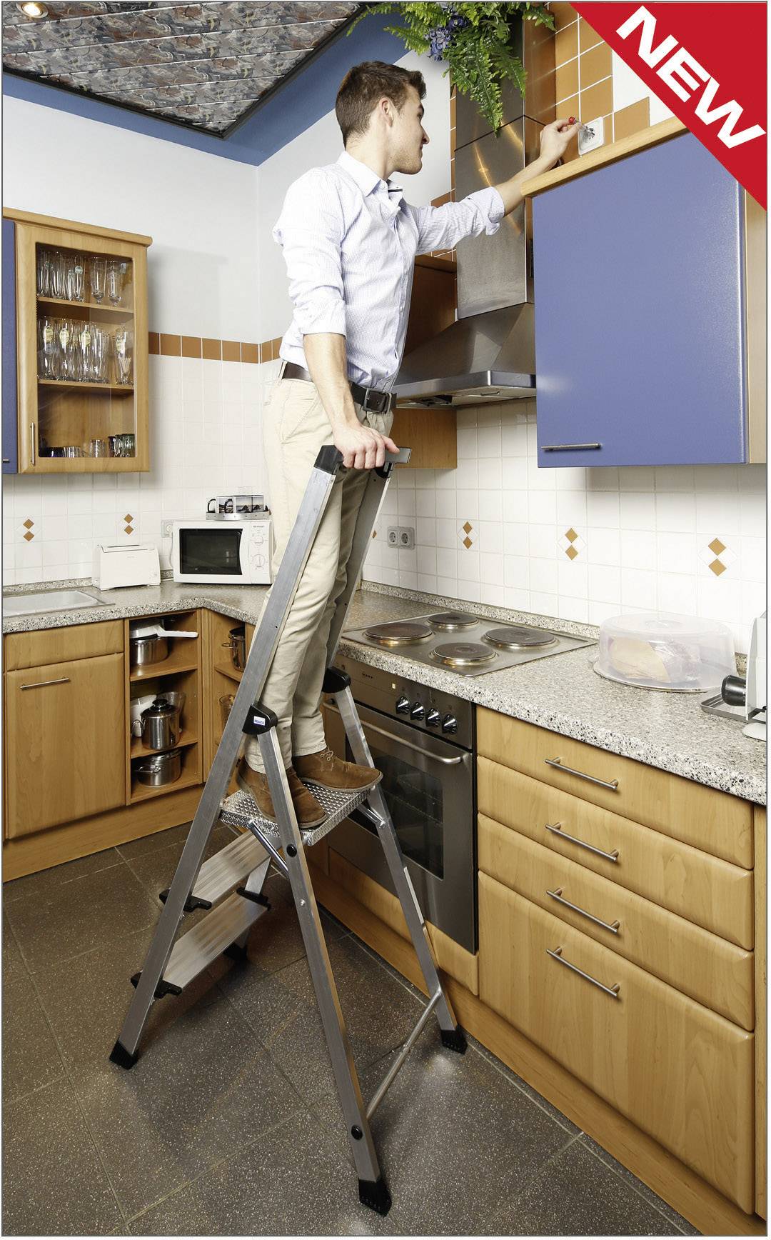 Een man staat op een vouwladder in een keuken en controleert een rookmelder aan het plafond. Links in het beeld bevinden zich keukenkastjes.