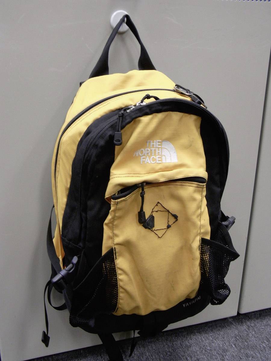 Een gele en zwarte rugzak hangt aan een haak. Op de voorkant staat 'The North Face'.