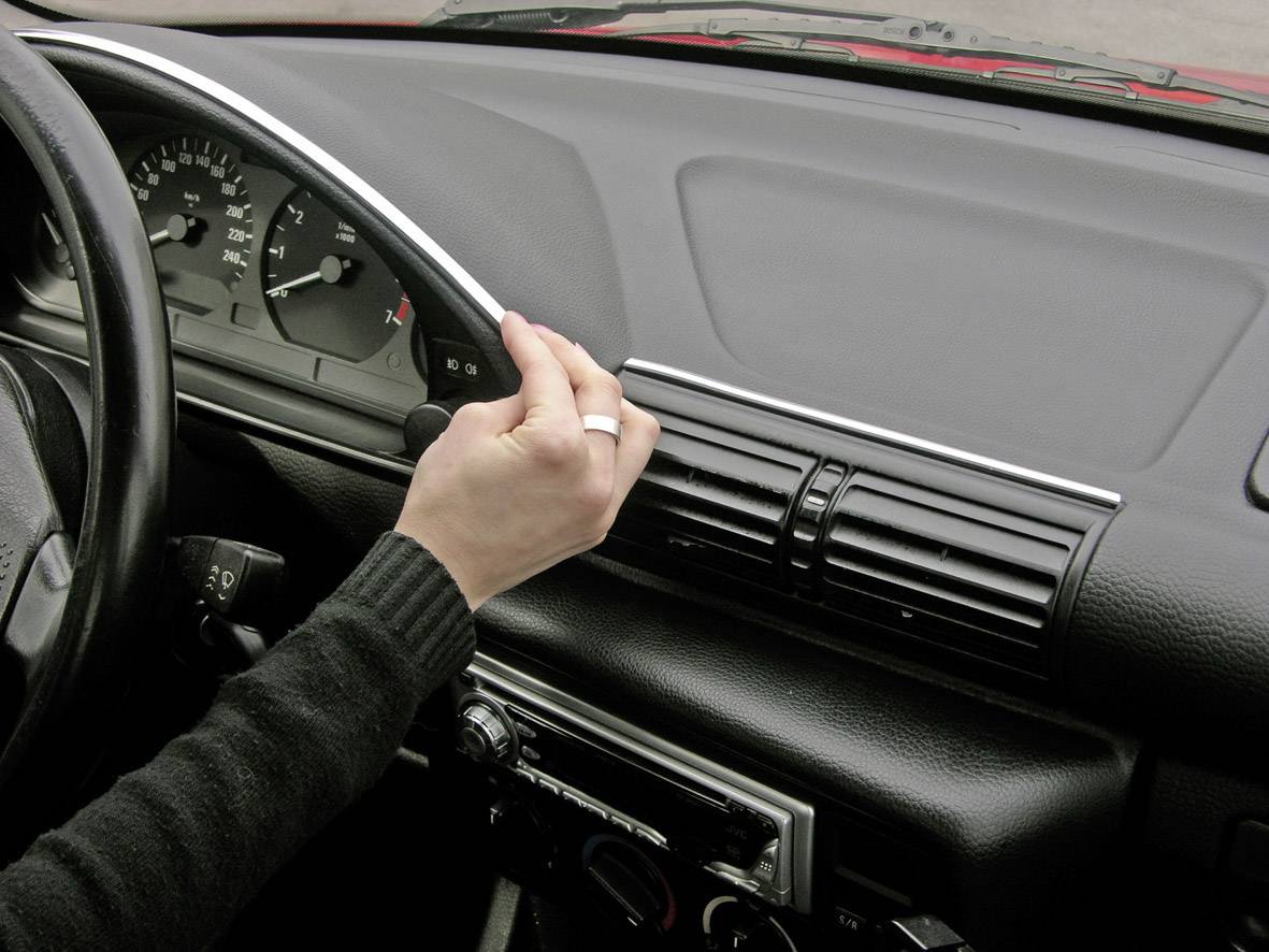 Een hand draait aan de ventilatieregelaar in het interieur van een auto. De bestuurder past de klimaatregeling aan.