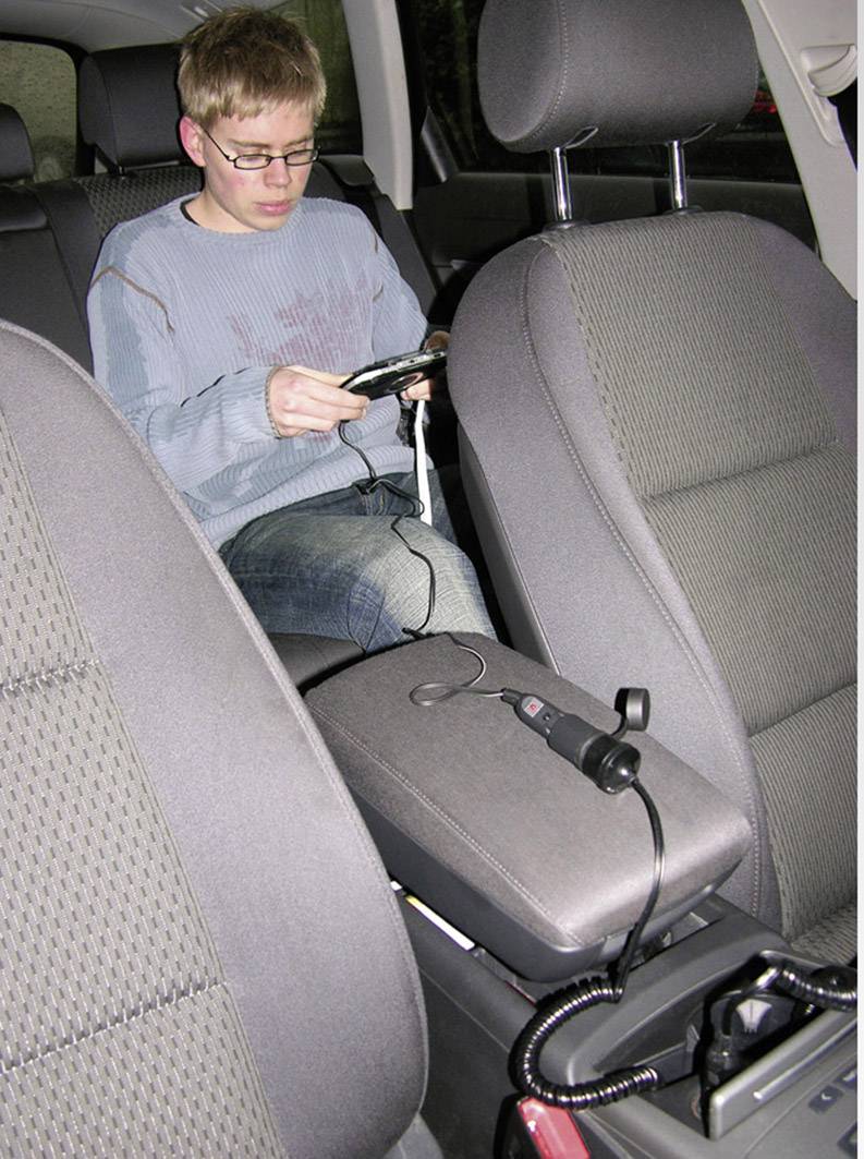 Een persoon zit op de achterbank van een auto en bekijkt een apparaat met snoeren. De bestuurdersstoel en middenconsole zijn zichtbaar.