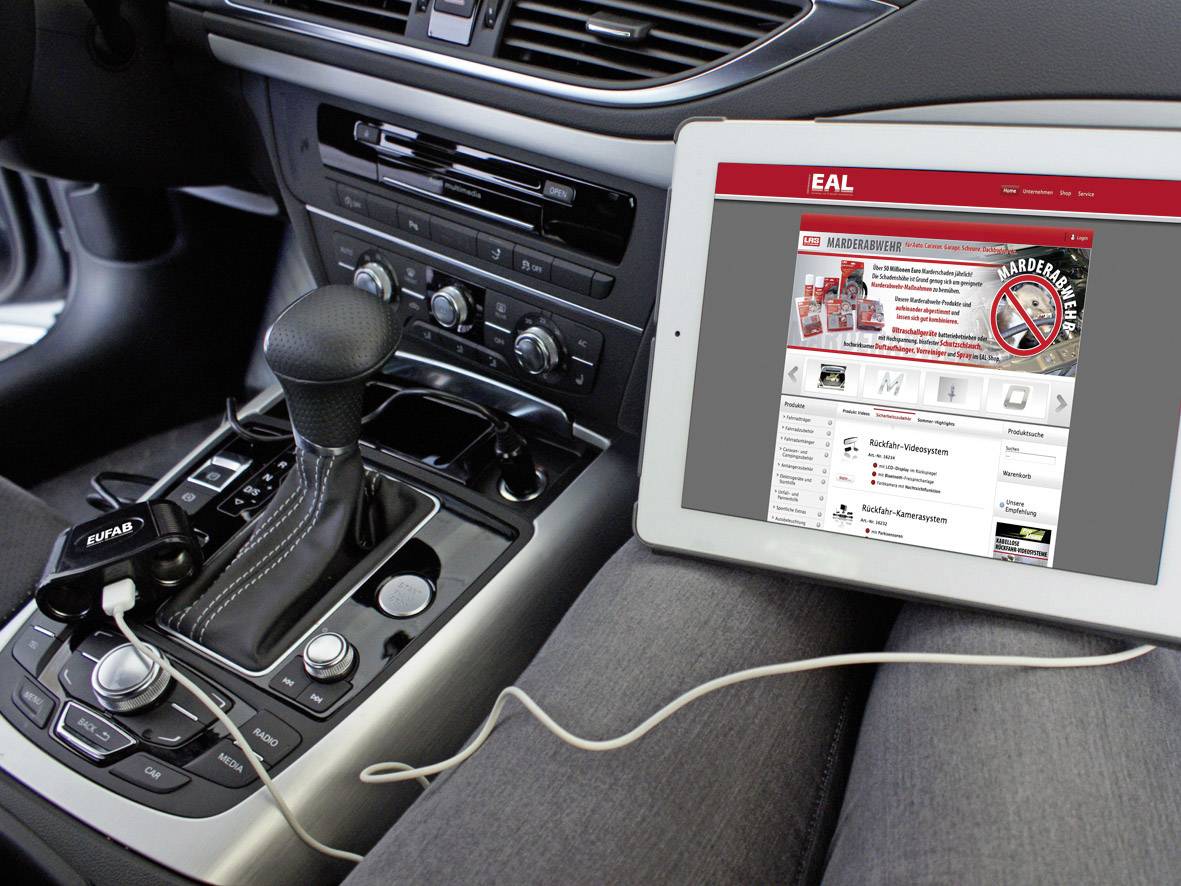 Een tablet toont de website van EAL op de schoot van een persoon in de auto, aangesloten op een oplader via USB in het dashboard.