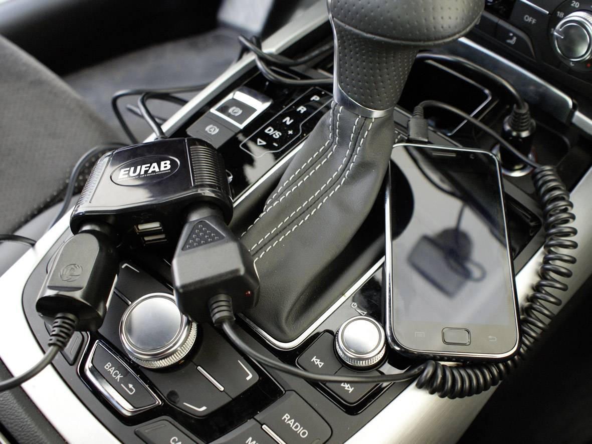 Smartphone met oplaadkabel naast de versnellingspook in de auto. Een EUFAB-laadstation met twee USB-poorten is eveneens aangesloten.