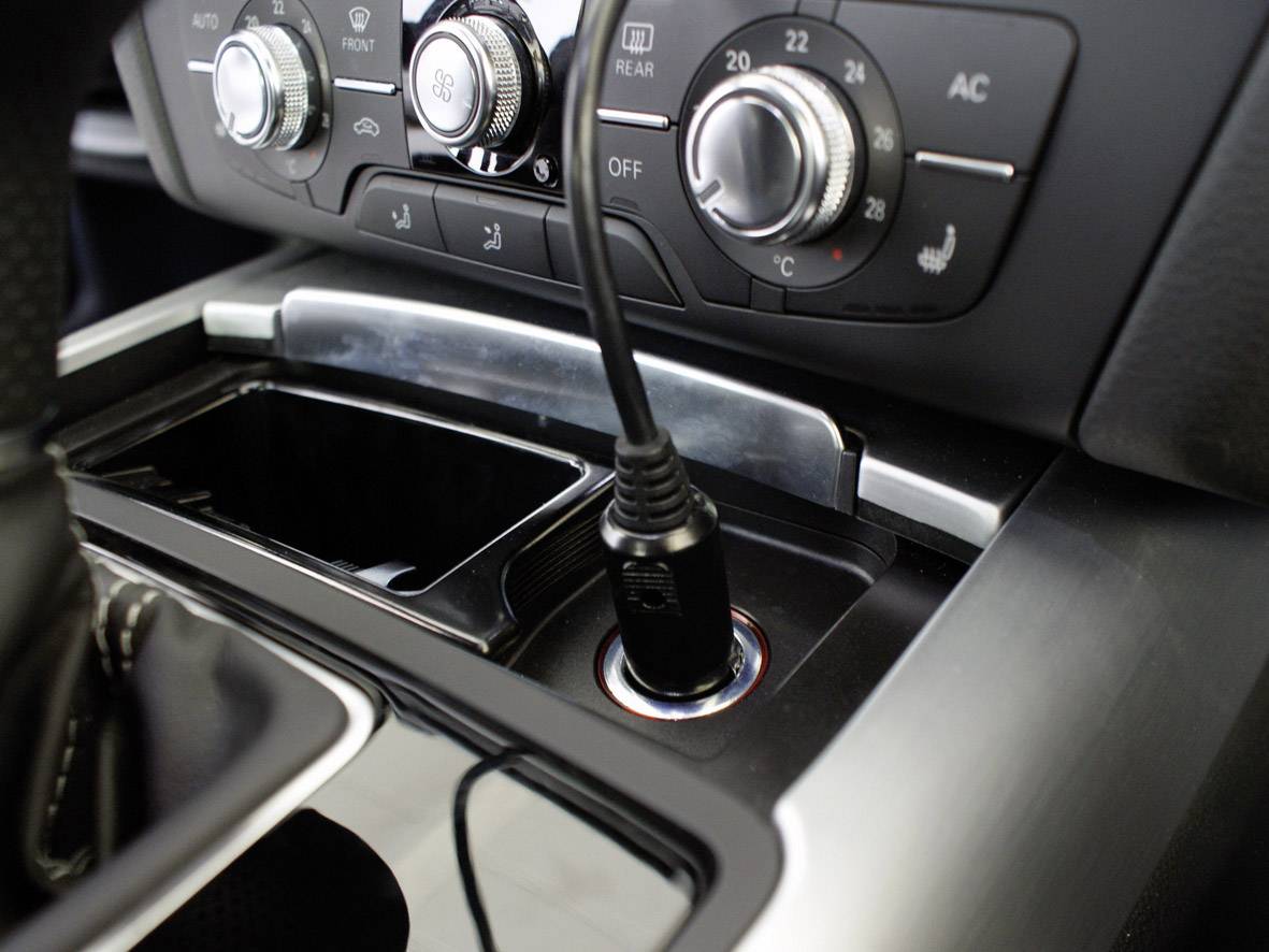 Het interieur van een auto toont een middenconsole met klimaatregelaars en een ingeplugd kabel in een oplaadaansluiting.
