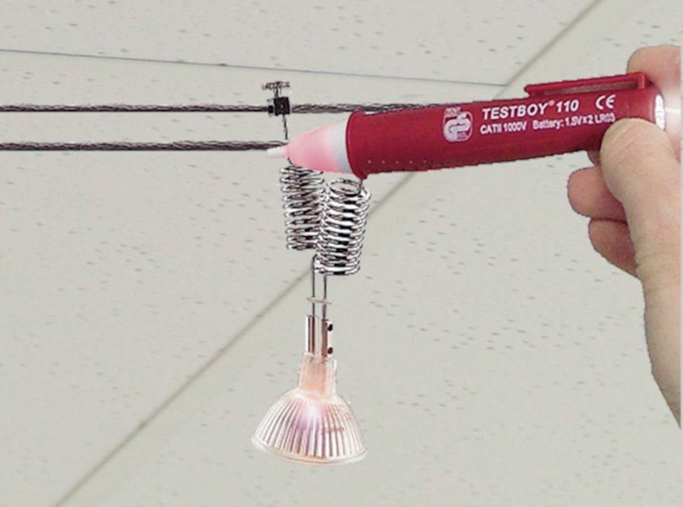 Een hand houdt een spanningszoeker tegen een draadkabel met een gemonteerde lamp om de spanning te controleren.