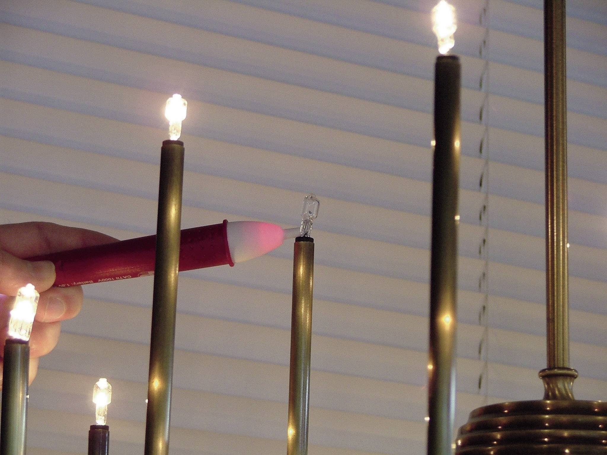 Een hand houdt een rode sigaret vast die op een gloeilamp is gericht, voor een raam met jaloezieën.