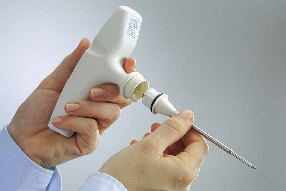Twee handen houden een medisch injectie-instrument vast. Eén hand draait een onderdeel van het apparaat los, waarschijnlijk ter voorbereiding of onderhoud.