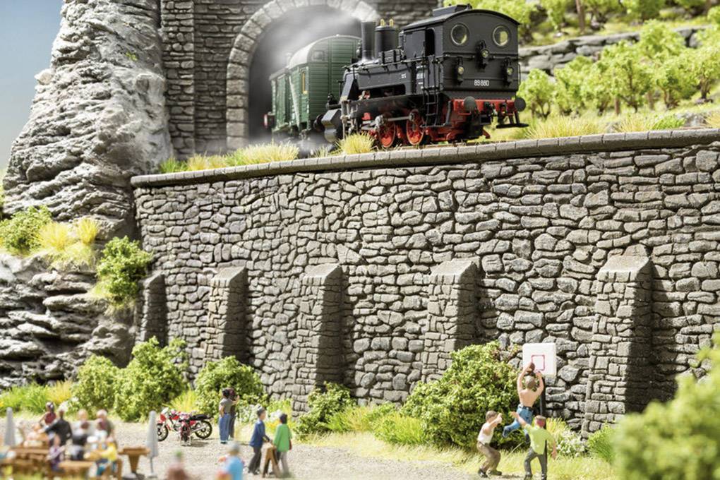 Een zwarte stoomlocomotief rijdt uit een tunnel in een modelspoorbaan-landschap, terwijl figuren daaronder basketbal aan het spelen zijn.