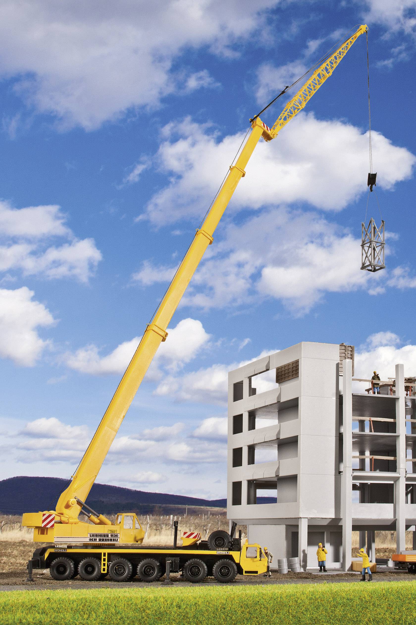Een gele mobiele kraan tilt een metalen onderdeel op voor een half afgebouwd gebouw. Bouwvakkers werken op de bovenste verdieping.