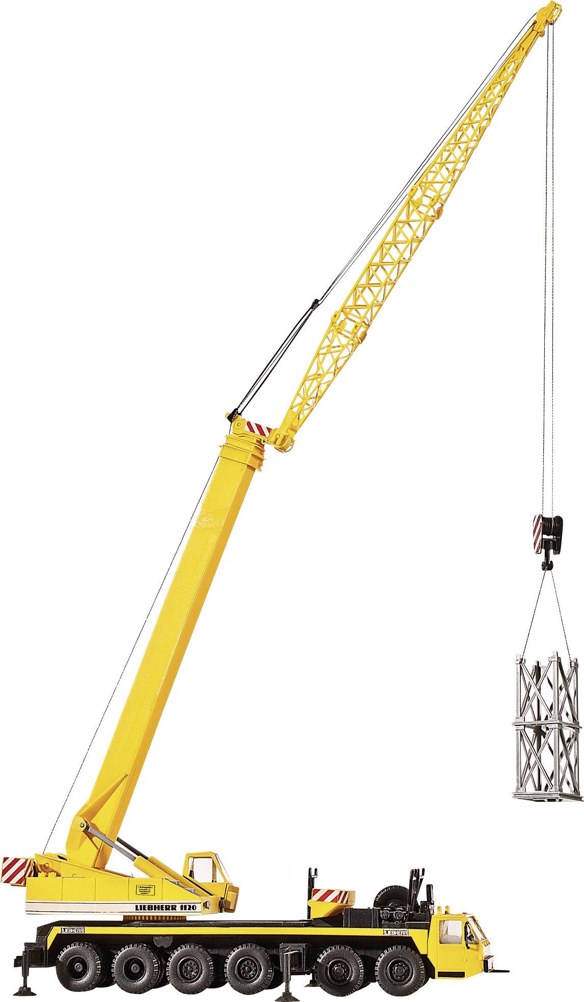 Een grote gele mobiele kraan tilt een metalen frame de lucht in. De kraan heeft meerdere assen en een lange uitlegger.