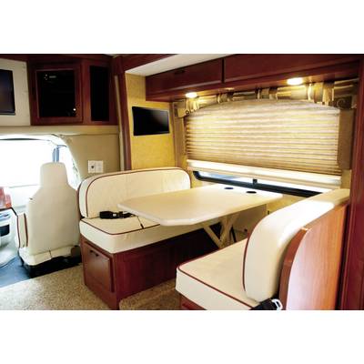 Een camper-interieur met een eettafel tussen twee zitbanken. Daglicht valt naar binnen door een raam met houten jaloezieën.