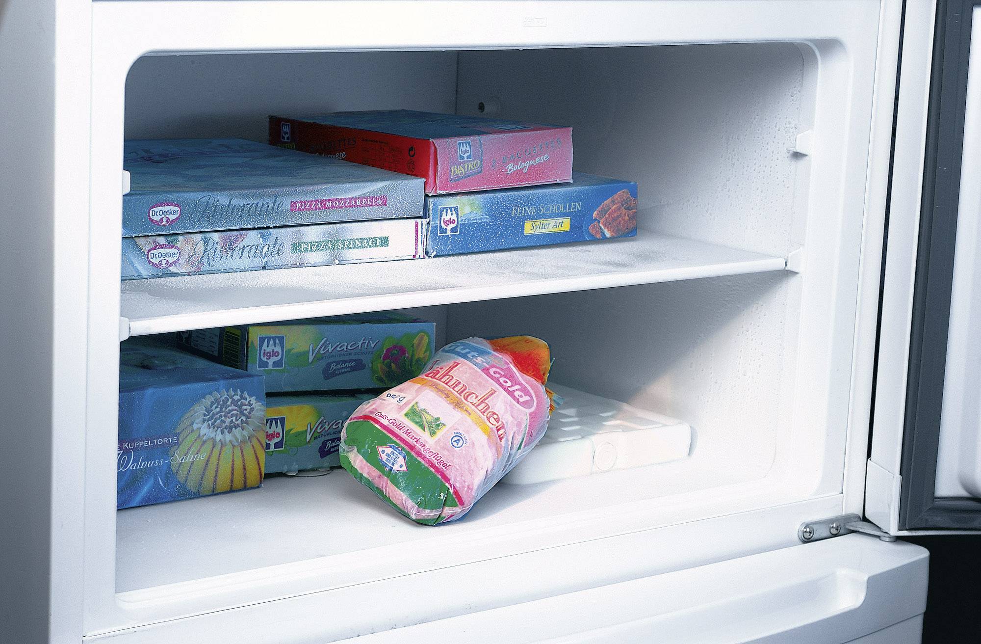 Een vriezer met verschillende diepvriesproducten op twee schappen. De deur staat een beetje open.