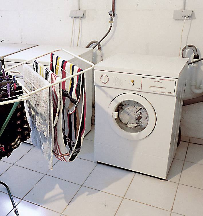 Wasmachine en droogrek met kleurrijke handdoeken op een betegelde vloer in een bijkeuken.