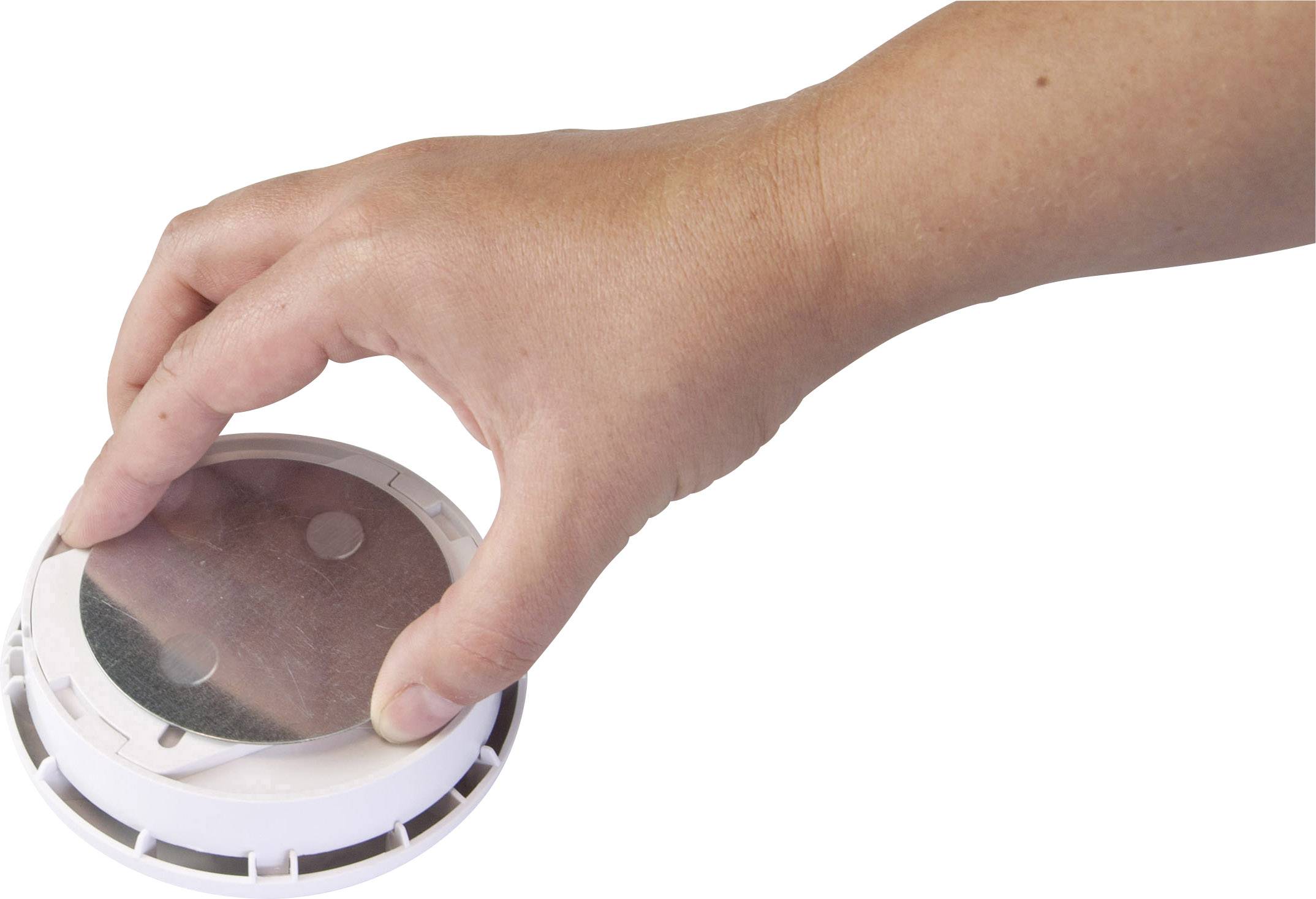 Hand plaatst een rond rookdetector aan het plafond. De rookmelder heeft een gladde, witte oppervlakte.