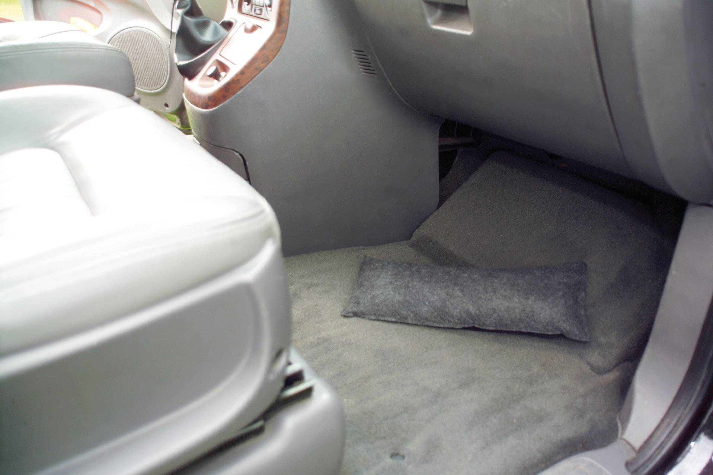 De afbeelding toont de vloerruimte van de bijrijdersstoel in een auto met een klein kussen op de vloer. Het gebied is schoon en netjes.