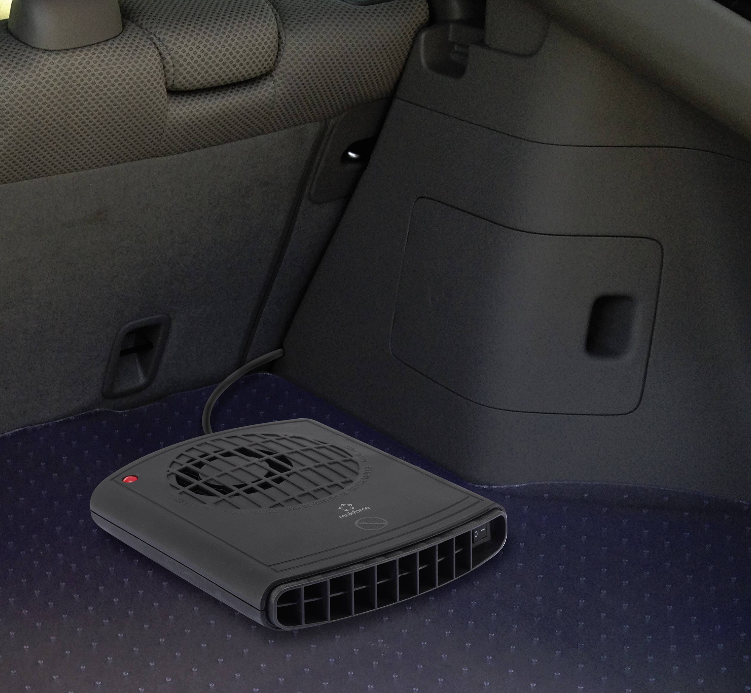 Een kleine, zwarte verwarmingsventilator staat op de vloer van een auto, dicht bij een stoel. Hij is gepositioneerd met de luchtinlaat naar voren gericht.