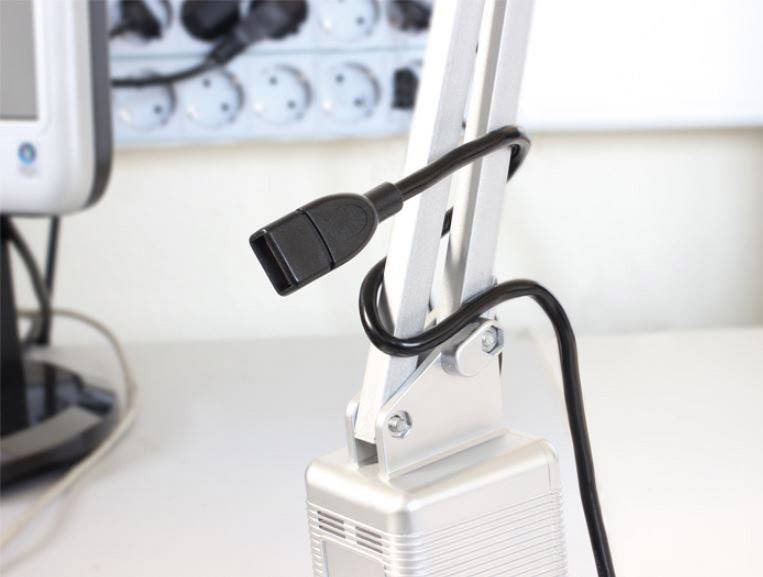 Een zwarte kabelverbinding loopt langs een witte lamp, op de achtergrond is een deel van een monitor zichtbaar.