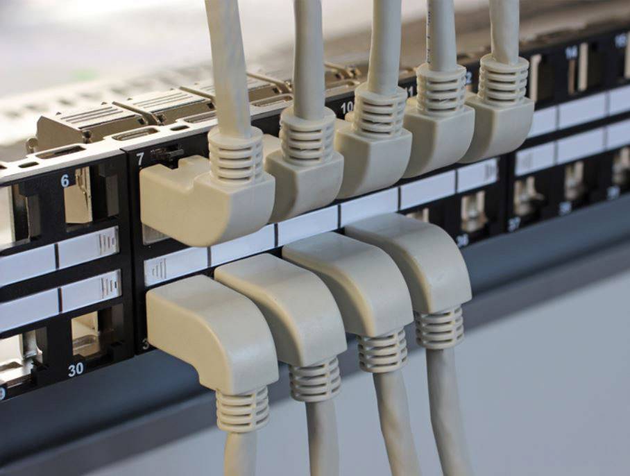Een netwerppaneel met acht aangesloten Ethernet-kabels die netjes in poorten op een serverrek zijn gestoken.