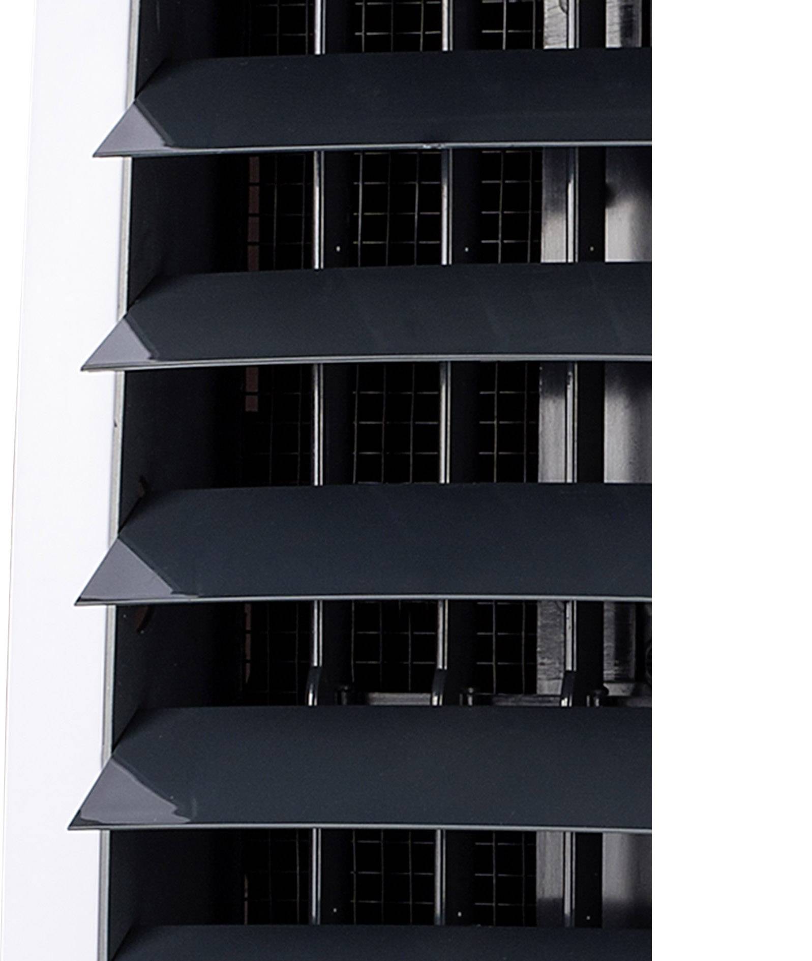 Close-upfoto van diagonale ventilatieschoepen van een airconditioningtoestel, gedeeltelijk geopend om luchtstroom mogelijk te maken.