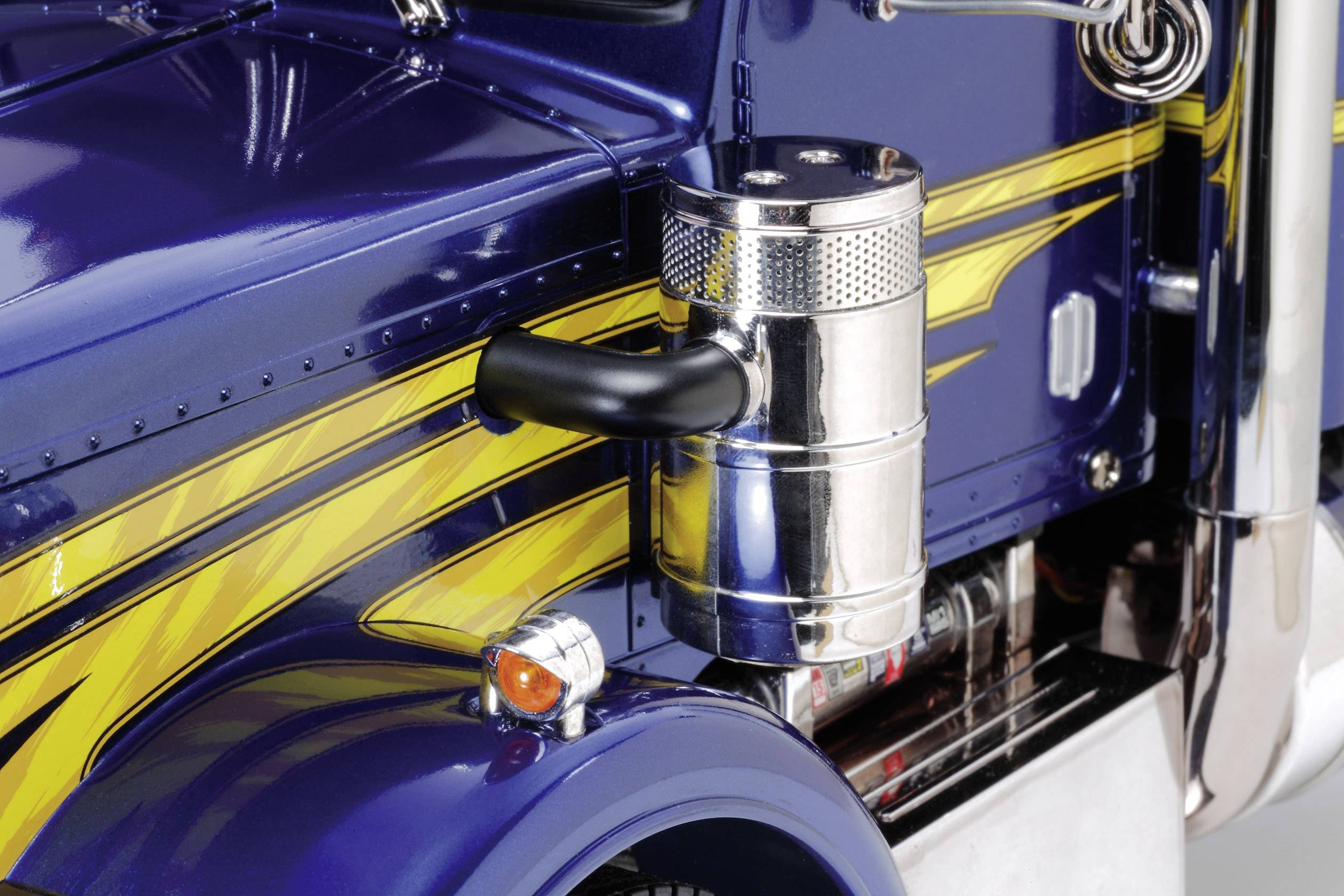 Blauwe vrachtwagen met gele versiering, close-up van de voorkant. Chromen details en een zilveren cilinder aan de zijkant.