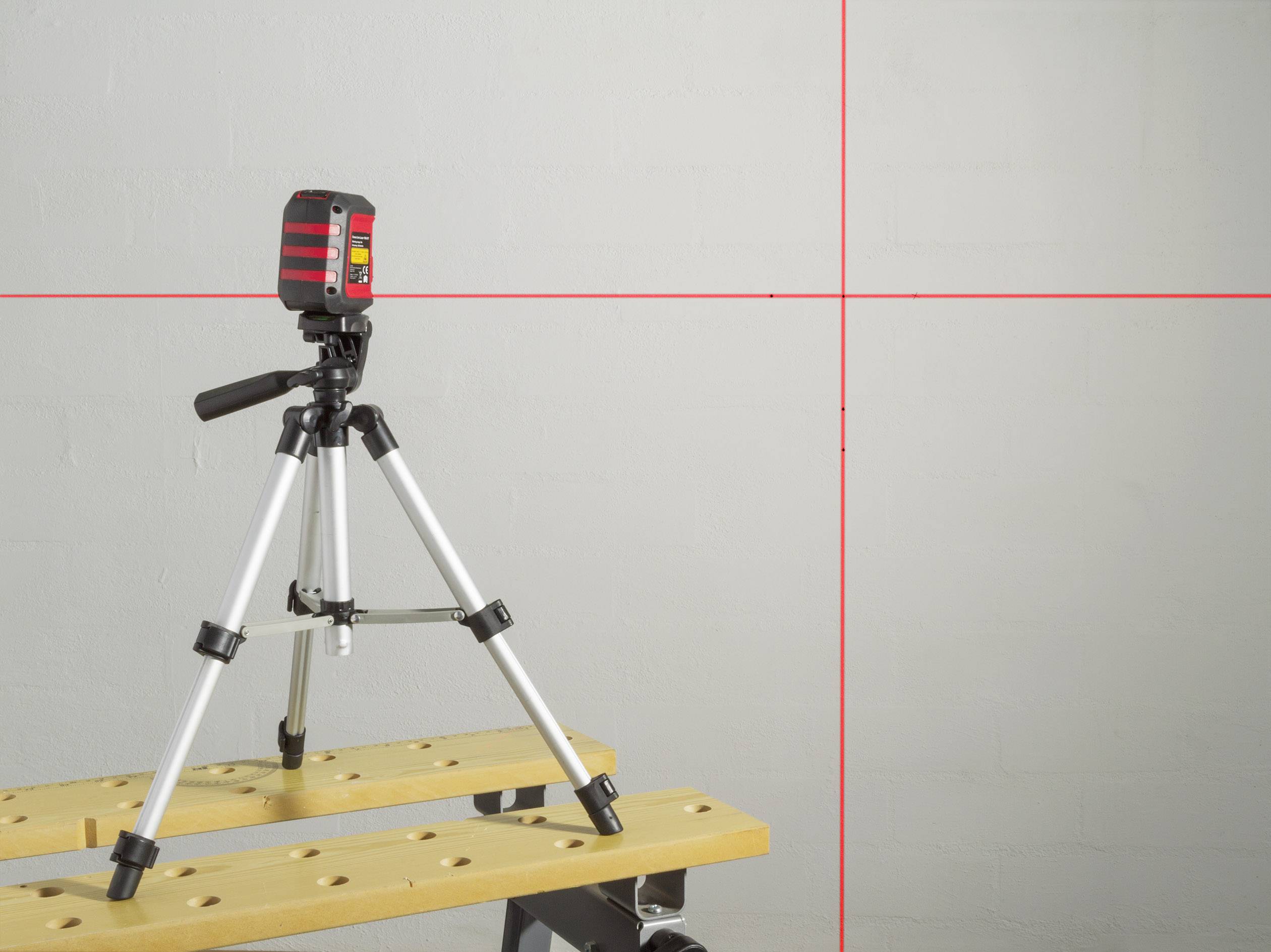 Een laserwaterpas op een statief projecteert rode lijnen op een muur en geeft horizontale en verticale uitlijningen aan.