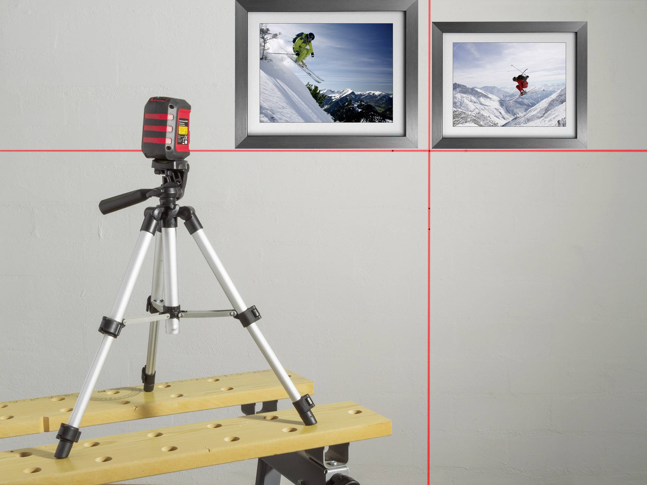 Een statief met een lasertoestel projecteert lijnen op een muur met twee foto's die skiërs in actie in met sneeuw bedekte bergen tonen.