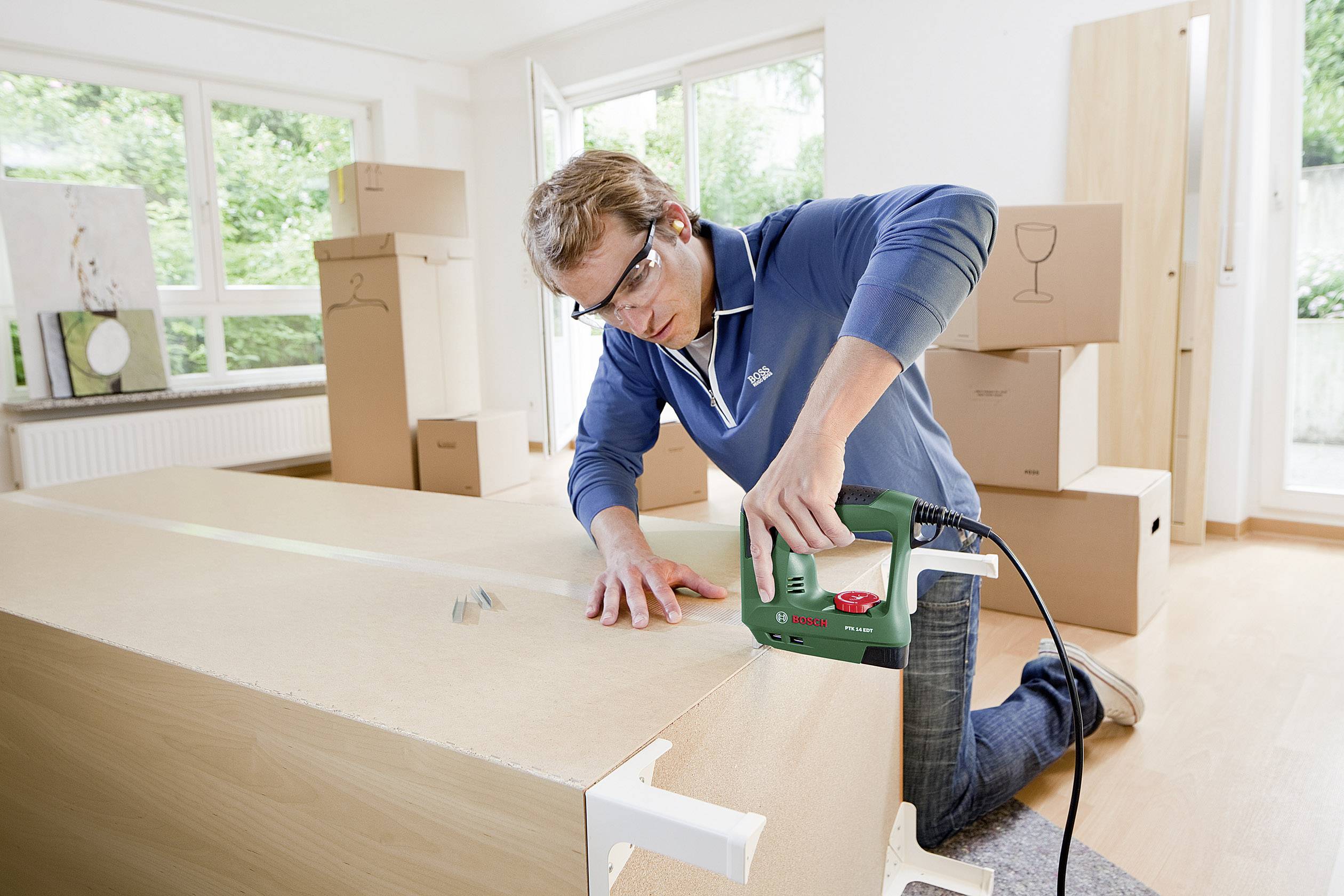 Een persoon monteert meubels in een lichte ruimte met veel verhuisdozen.