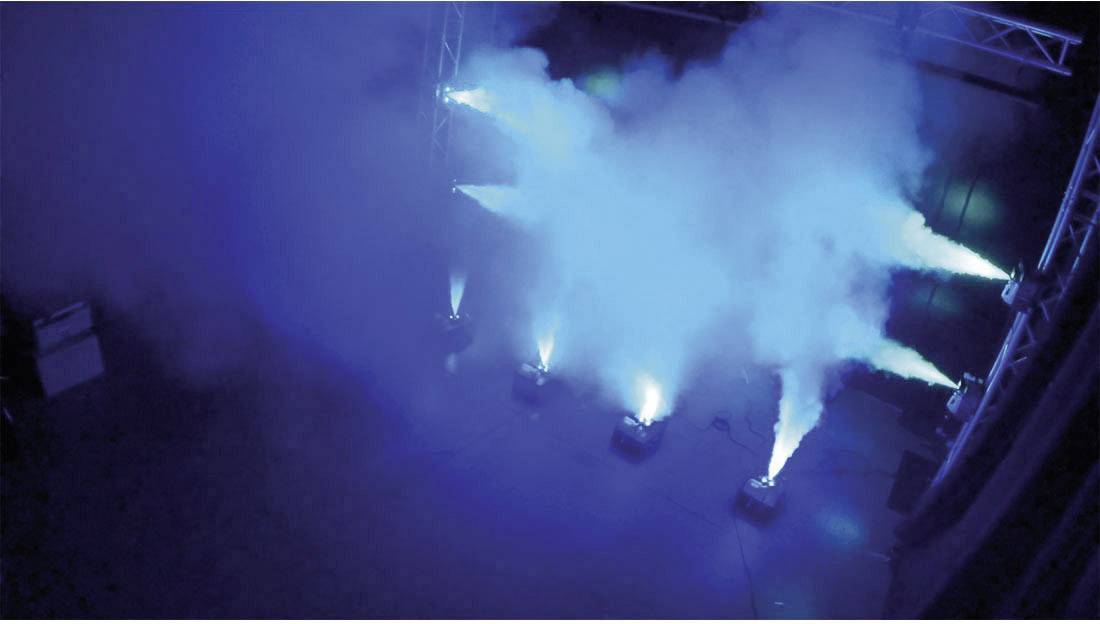 Vijf schijnwerpers stralen diepblauw licht uit op een podium in een donkere ruimte, omgeven door mist.
