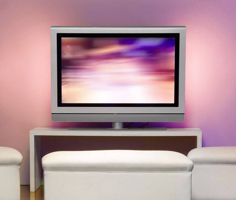 Flatscreen-tv op een tafel met diffuse roze verlichting op de achtergrond, een vaag beeld op het scherm.