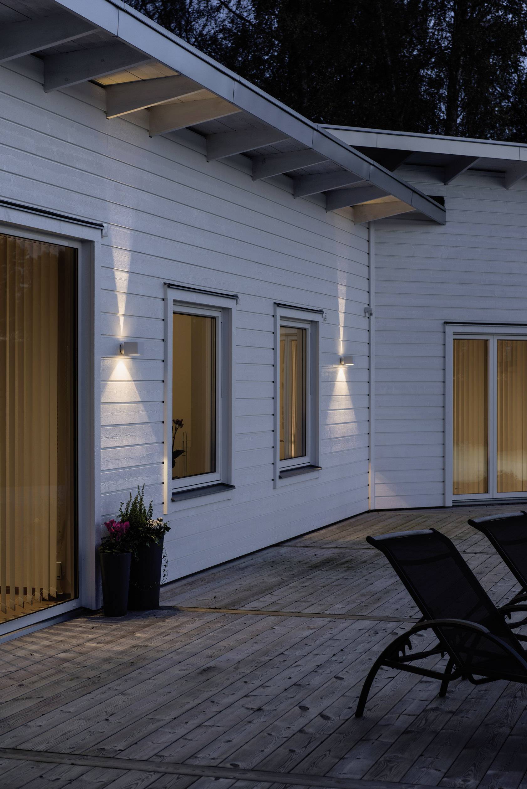 Modern wit houten huis bij schemering. Buitenverlichting is ingeschakeld en geeft het gebouw een uitnodigende sfeer.