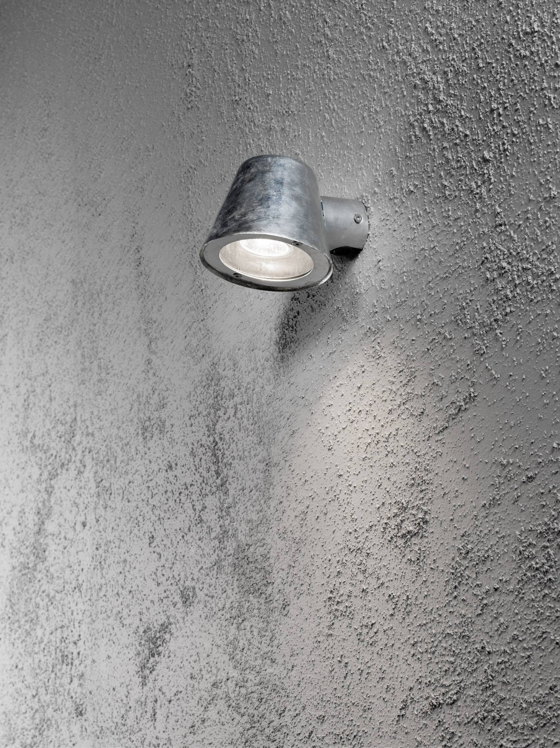 Buitenlamp van metaal gemonteerd aan een gestructureerde muur, schijnt naar beneden.