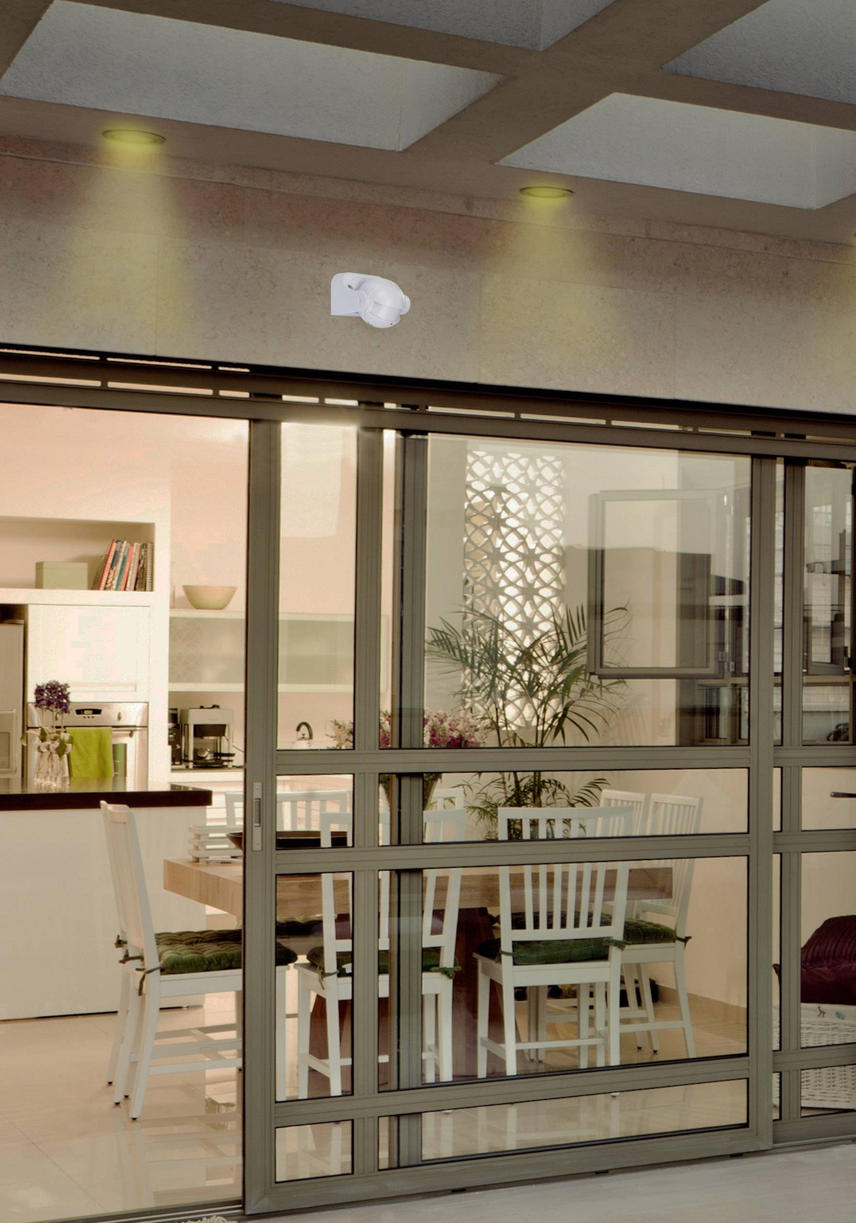 Eetkamer met glazen wanden, houten tafel, witte stoelen en zicht op de keuken. Modern, gezellig interieur bij gedempt licht.