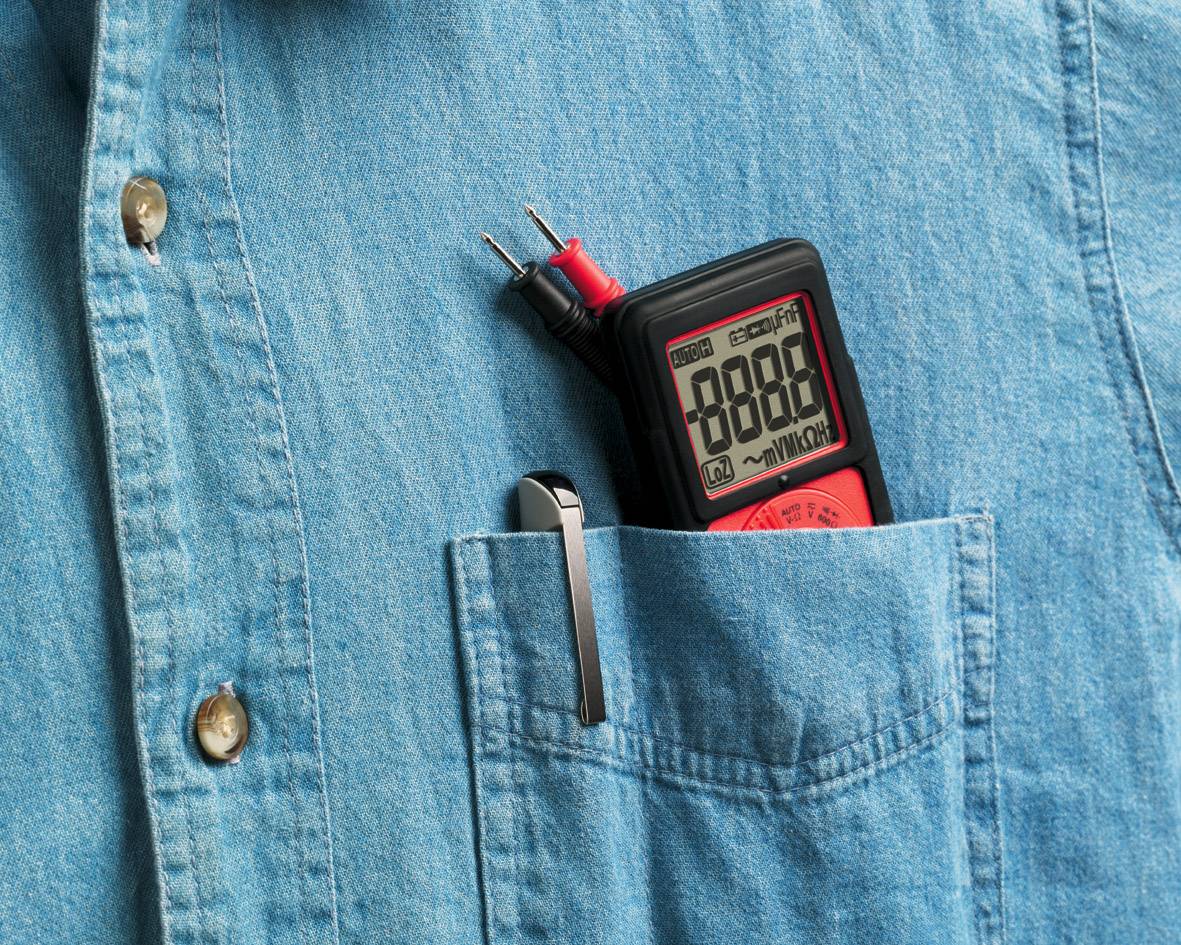 Een multimeter steekt in de borstzak van een blauw overhemd. Het toont '8888' op het display. Ernaast steekt een pen.
