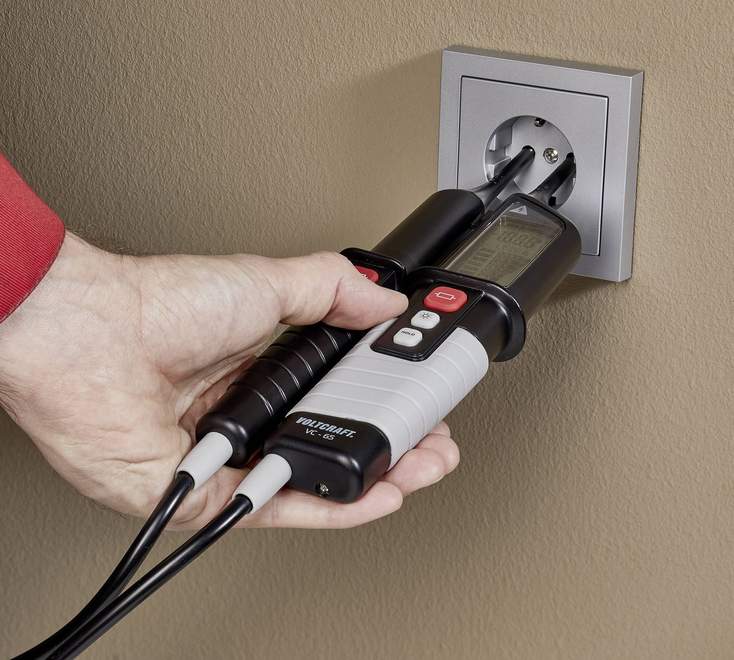 Een hand houdt een spanningszoeker vast die in een stopcontact wordt gestoken om de elektrische stroom te meten.