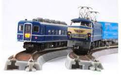 Twee modelltreinen op gebogen rails bewegen zich naar elkaar toe. De voorste trein is blauw met gele details.