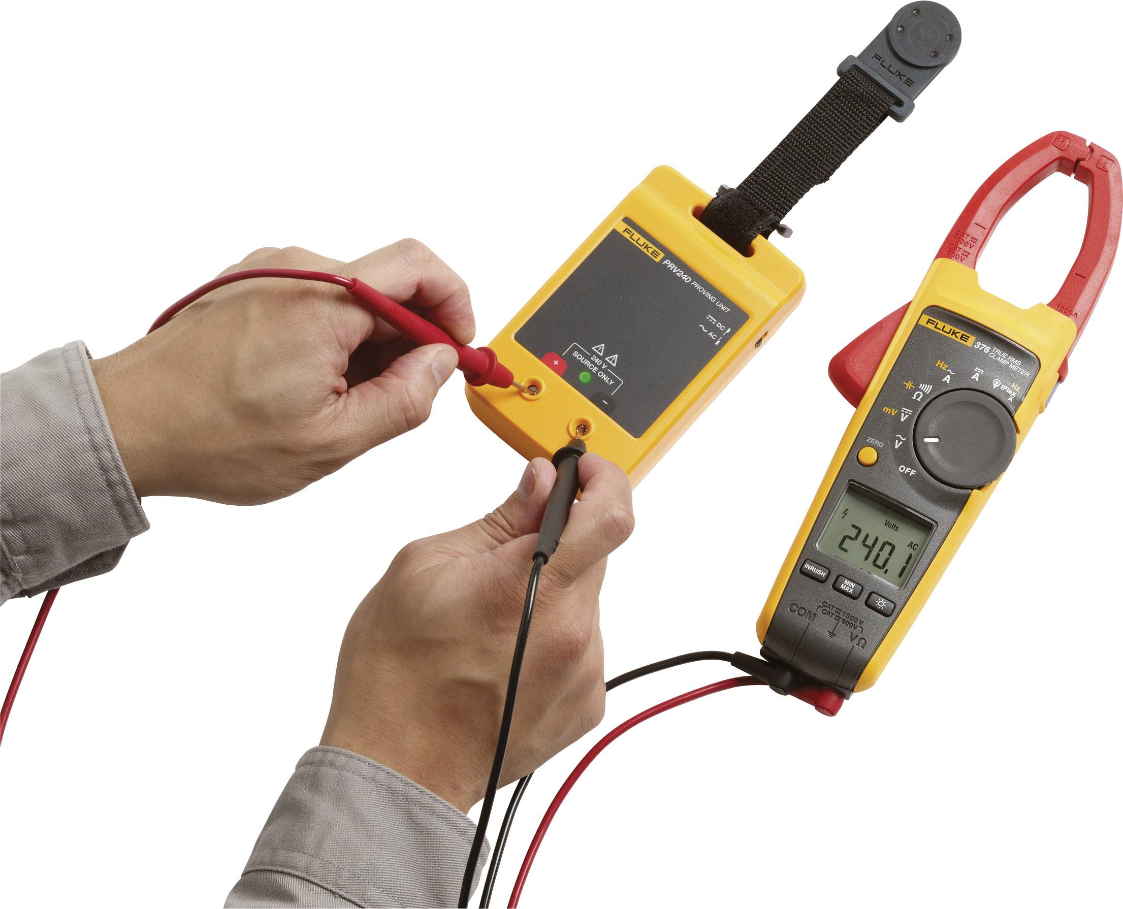 Twee handen bedienen een multimeter met een digitale weergave van 24,0, verbonden met een geel testapparaat.