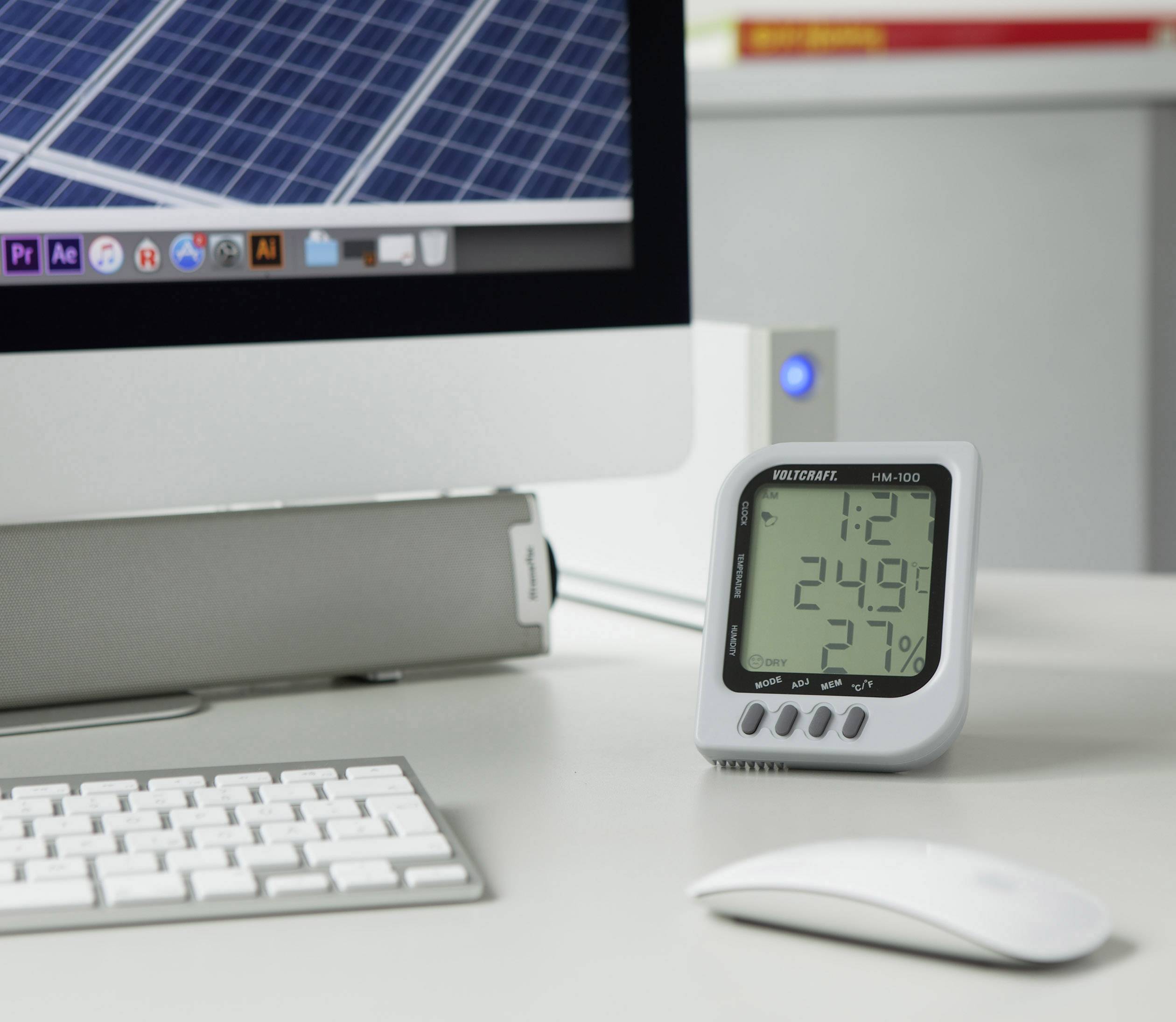 Op een bureau staat een digitale thermometer voor een computerscherm. Het toont 12°C en 24% luchtvochtigheid.