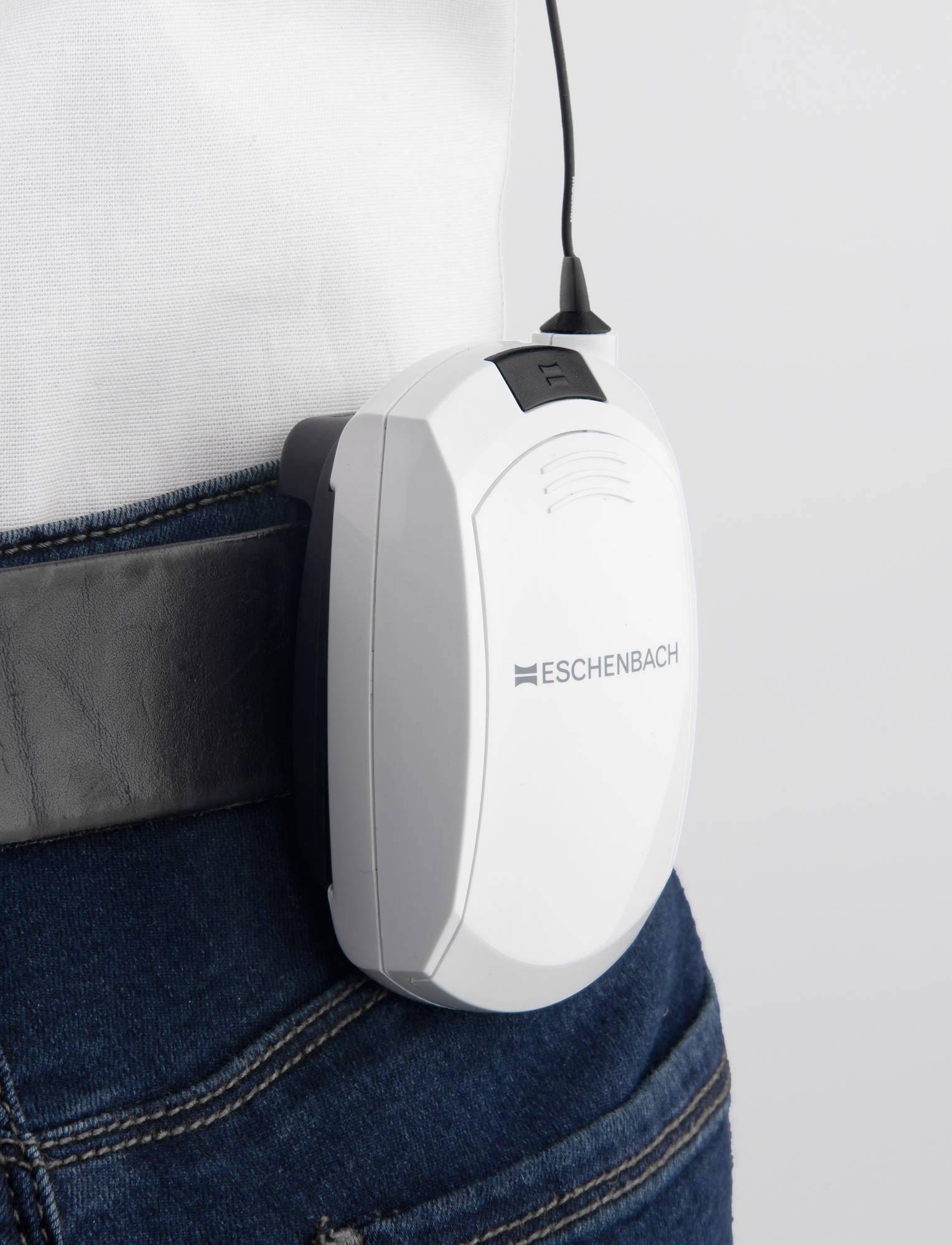 Een draagbaar klein wit apparaat met de naam 'Eschenbach' is aan een riem bevestigd. Het heeft een antenne en dient vermoedelijk voor communicatie of meting.