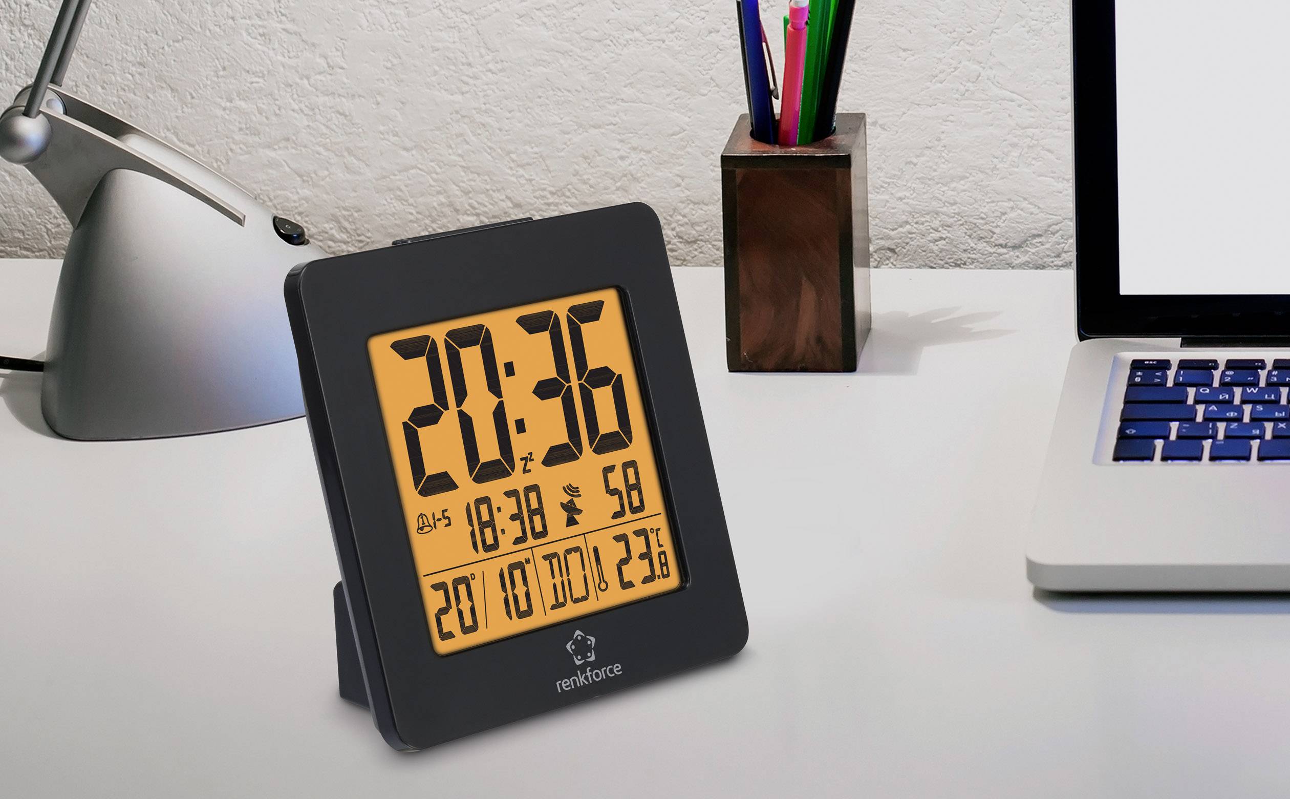 Digitale klok op een bureau toont 20:36. Datum, temperatuur en luchtvochtigheid worden eveneens weergegeven. Links een bureaulamp, rechts een laptop.