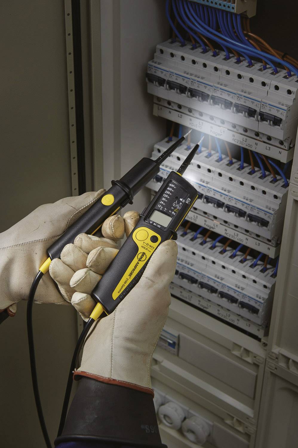 Een elektricien met beschermende handschoenen gebruikt een digitale multimeter om stroom te controleren in een geopende schakelkast.