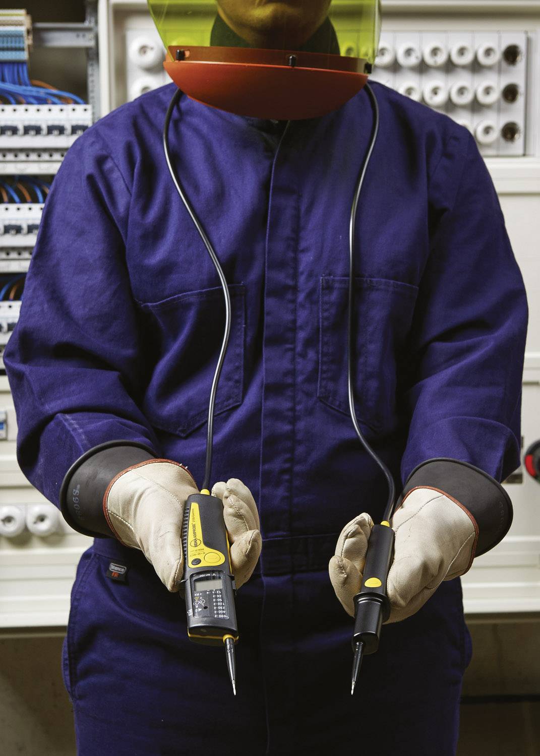 Elektricien in beschermende werkkleding houdt een spanningzoeker voor een elektrische schakelkast.