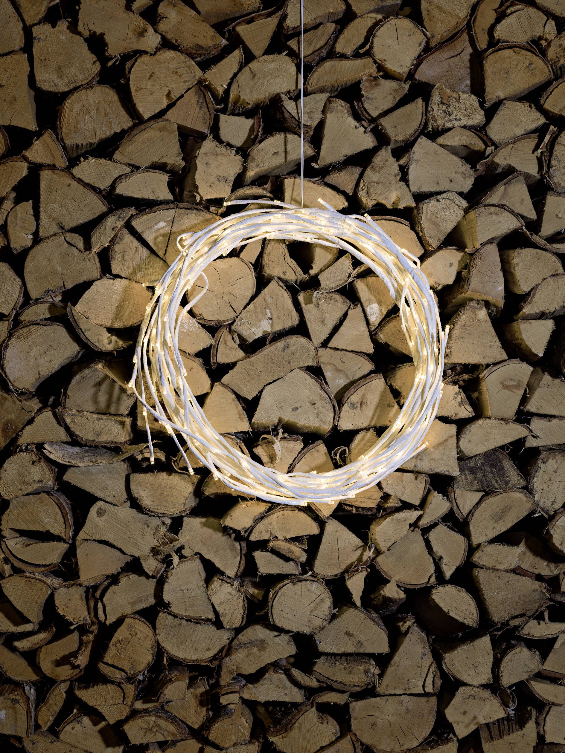 Een krans van schitterende lichten hangt voor een achtergrond van gestapeld brandhout, die gezelligheid uitstraalt.