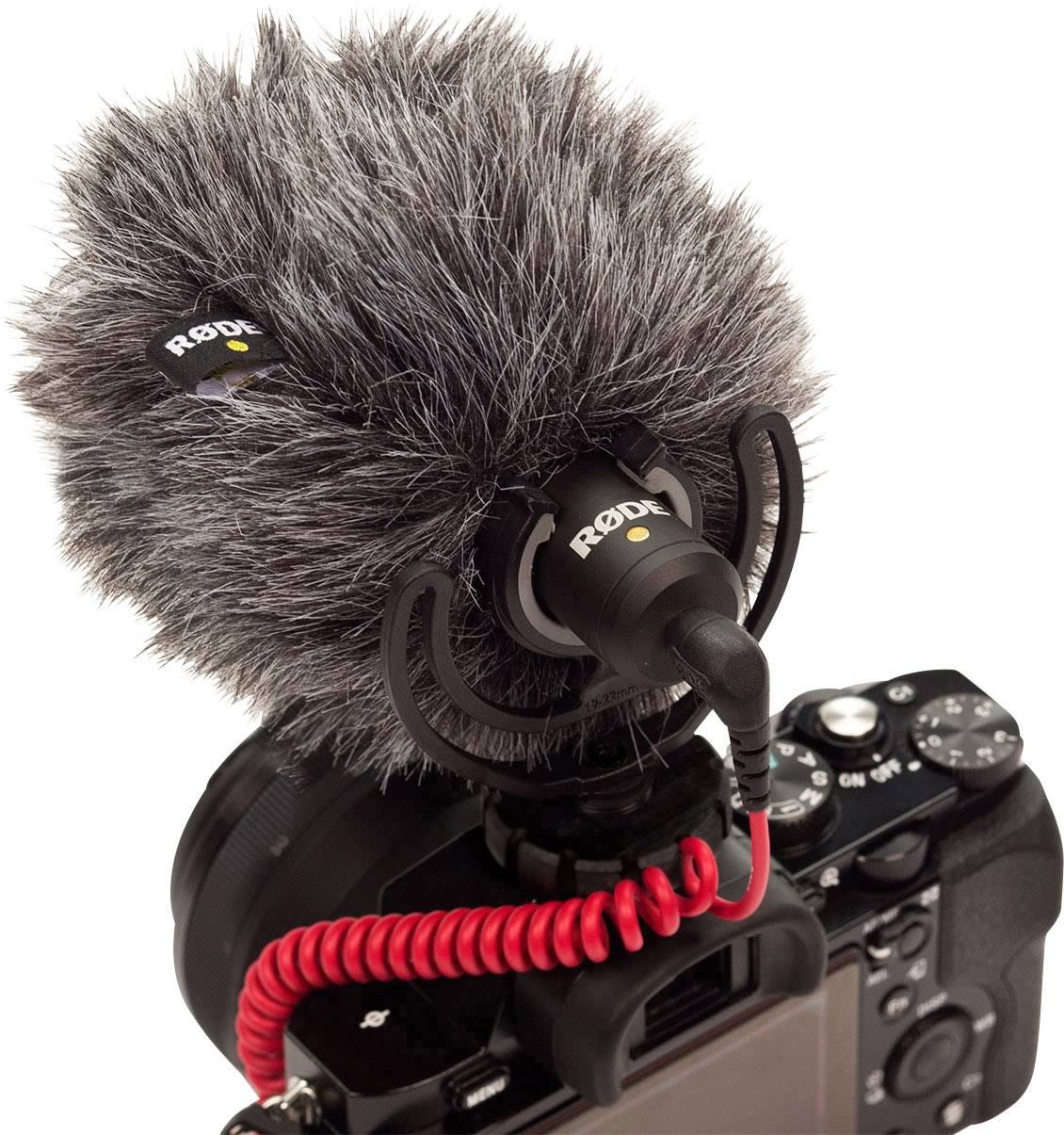 Een microfoon met een grijze windkap is bovenop een zwarte camera bevestigd. Een rood snoer verbindt beide apparaten.